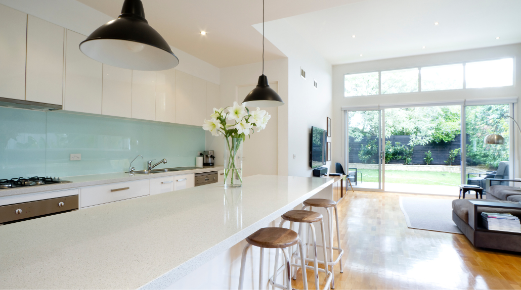 Open plan kitchen with stone island benchtop, pendant lights and living area beyond